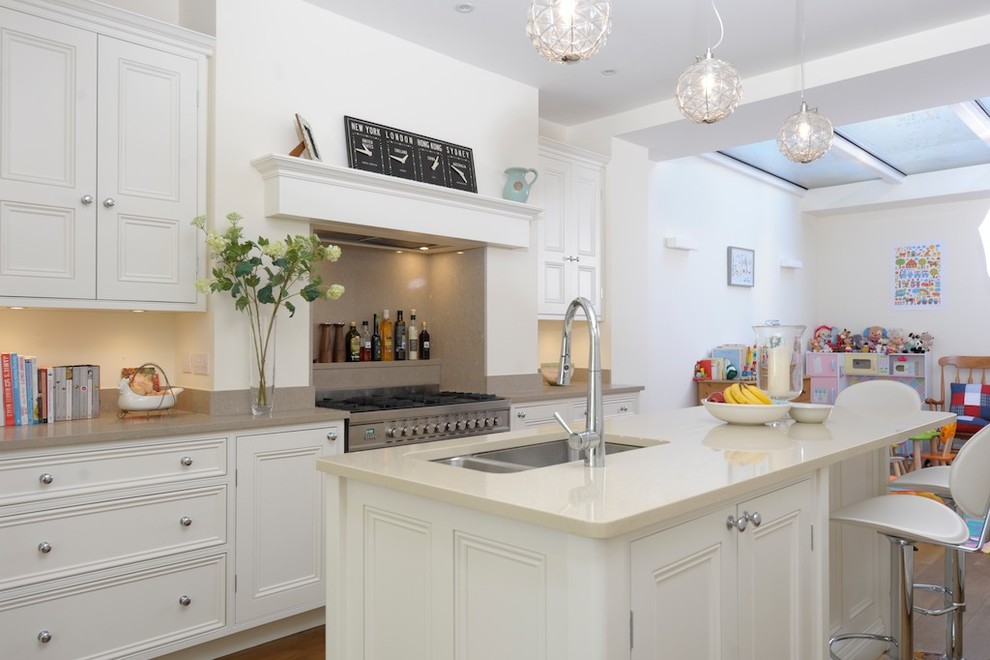 Design ideas for a large traditional galley open plan kitchen in London with a submerged sink, recessed-panel cabinets, white cabinets, granite worktops, stainless steel appliances, light hardwood flooring and an island.