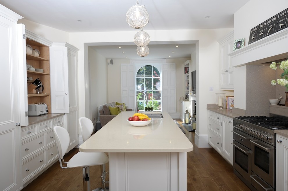 This is an example of a large traditional galley open plan kitchen in London with a submerged sink, recessed-panel cabinets, white cabinets, granite worktops, stainless steel appliances, light hardwood flooring and an island.
