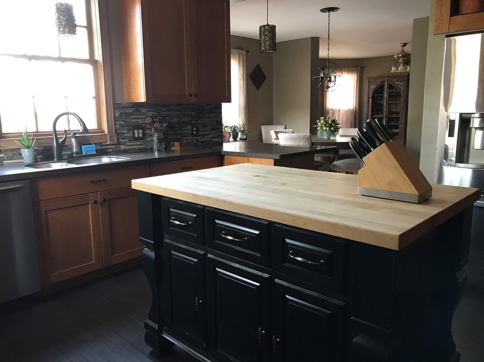 Ornate u-shaped ceramic tile and black floor eat-in kitchen photo in New York with an undermount sink, recessed-panel cabinets, medium tone wood cabinets, solid surface countertops, multicolored backsplash, glass tile backsplash, stainless steel appliances, an island and black countertops