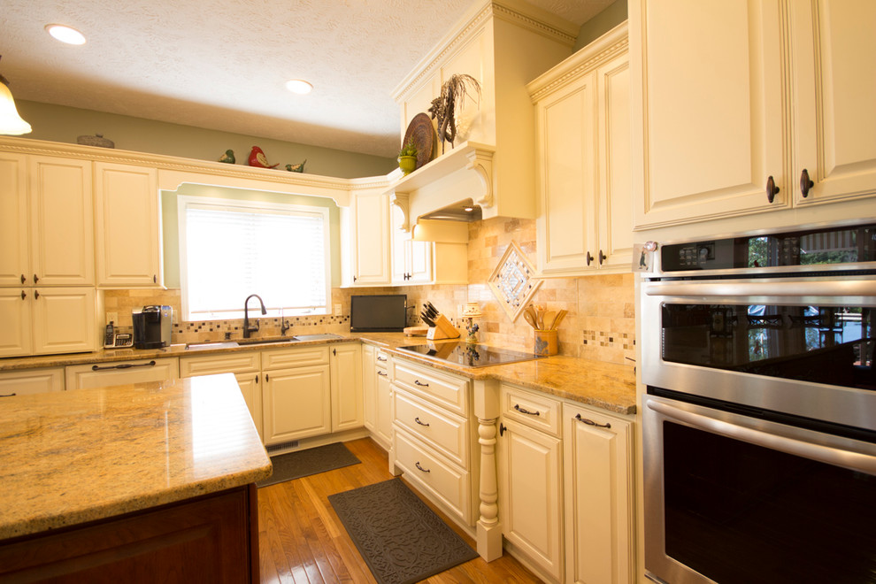 Cette photo montre une très grande cuisine ouverte chic en L avec des portes de placard blanches, un sol en bois brun, îlot, un placard avec porte à panneau surélevé et un électroménager en acier inoxydable.