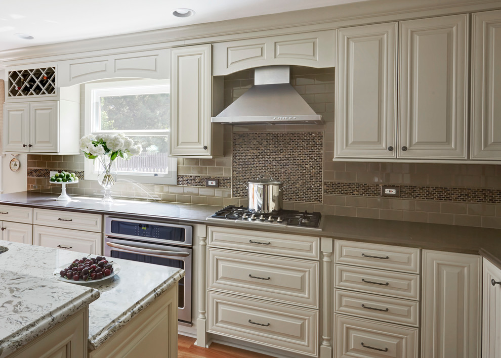 Klassisk inredning av ett mellanstort kök, med en enkel diskho, luckor med upphöjd panel, vita skåp, bänkskiva i kvarts, grått stänkskydd, stänkskydd i keramik, rostfria vitvaror, mellanmörkt trägolv och en köksö