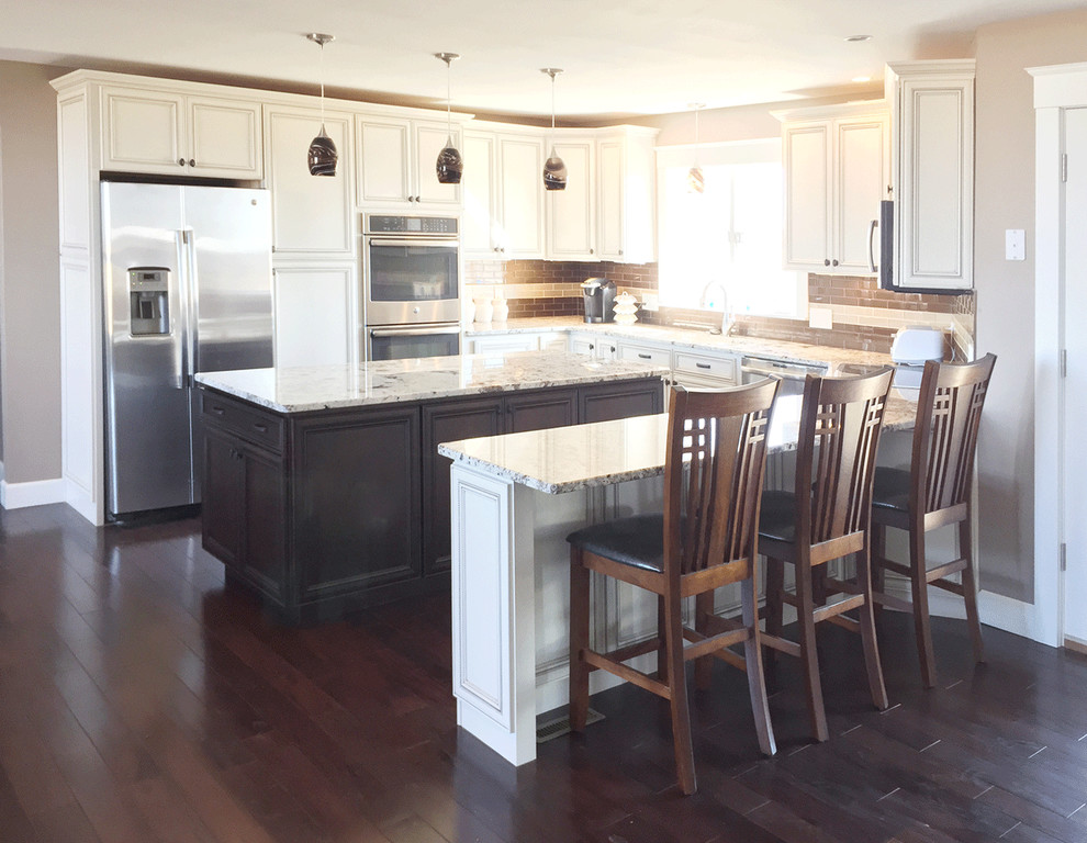 Example of a large classic l-shaped dark wood floor open concept kitchen design in Other with white cabinets, two islands, an undermount sink, recessed-panel cabinets, brown backsplash and stainless steel appliances