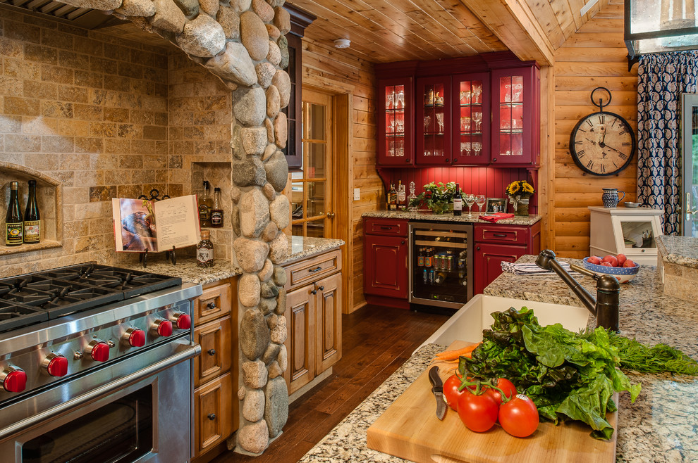 Cette image montre une grande cuisine ouverte traditionnelle en L avec un électroménager en acier inoxydable, un sol en bois brun, îlot, un évier de ferme, un placard avec porte à panneau encastré, des portes de placard rouges et une crédence beige.