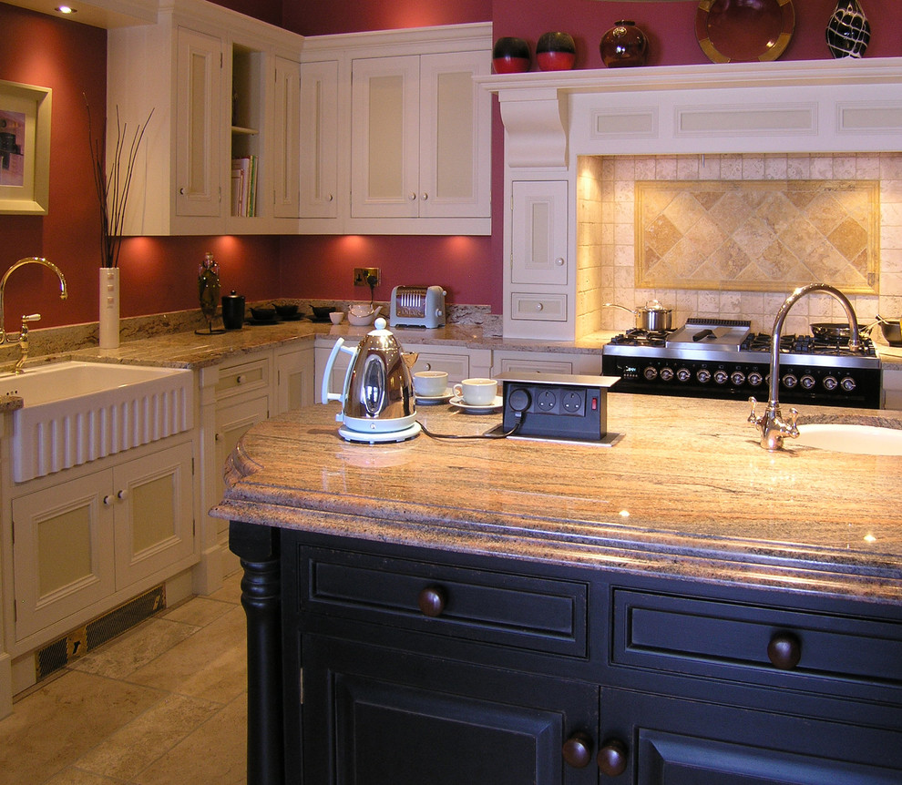 Klassisk inredning av ett mellanstort l-kök, med en rustik diskho, luckor med infälld panel, vita skåp, granitbänkskiva, beige stänkskydd, stänkskydd i keramik, travertin golv och en köksö