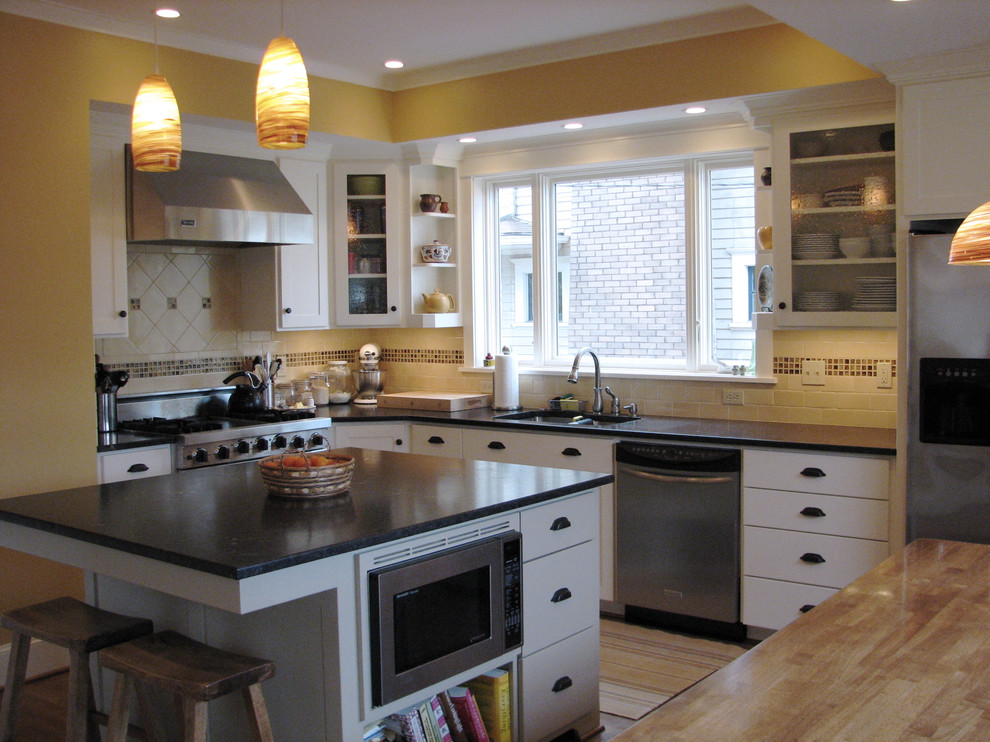 На фото: кухня в классическом стиле с белыми фасадами, разноцветным фартуком, фартуком из травертина и барной стойкой