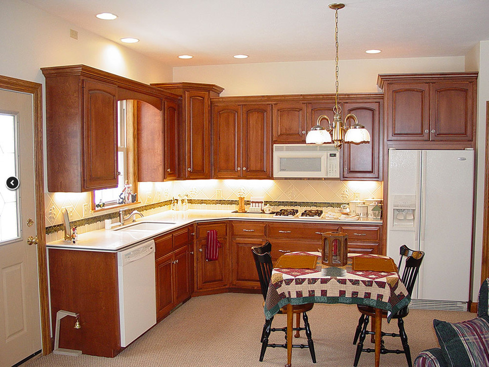 Mid-sized elegant l-shaped carpeted open concept kitchen photo in Cleveland with an undermount sink, beaded inset cabinets, medium tone wood cabinets, solid surface countertops, white backsplash, ceramic backsplash, white appliances and no island