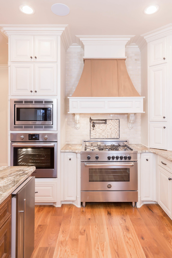 Exempel på ett klassiskt kök, med luckor med upphöjd panel, vita skåp, vitt stänkskydd, rostfria vitvaror och mellanmörkt trägolv