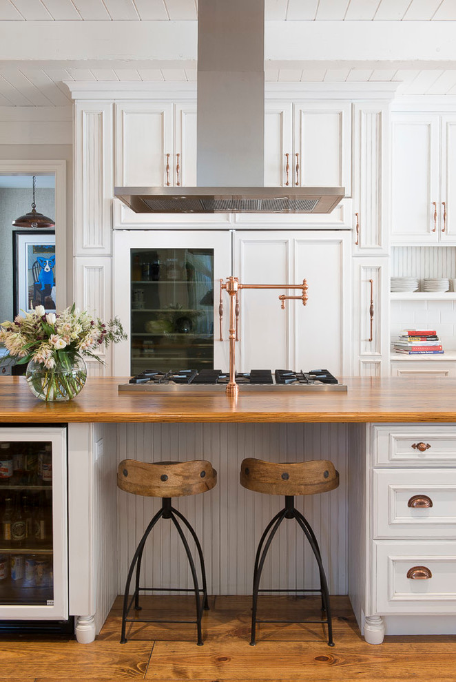 Klassisk inredning av ett kök, med luckor med infälld panel, vita skåp, träbänkskiva, integrerade vitvaror, mellanmörkt trägolv och en köksö