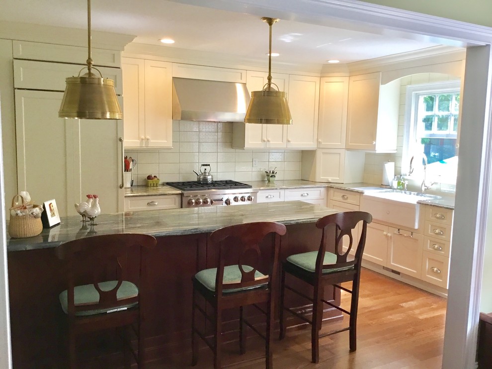 This is an example of a medium sized traditional u-shaped enclosed kitchen in New York with a belfast sink, recessed-panel cabinets, white cabinets, quartz worktops, beige splashback, ceramic splashback, stainless steel appliances, dark hardwood flooring, an island, brown floors and white worktops.