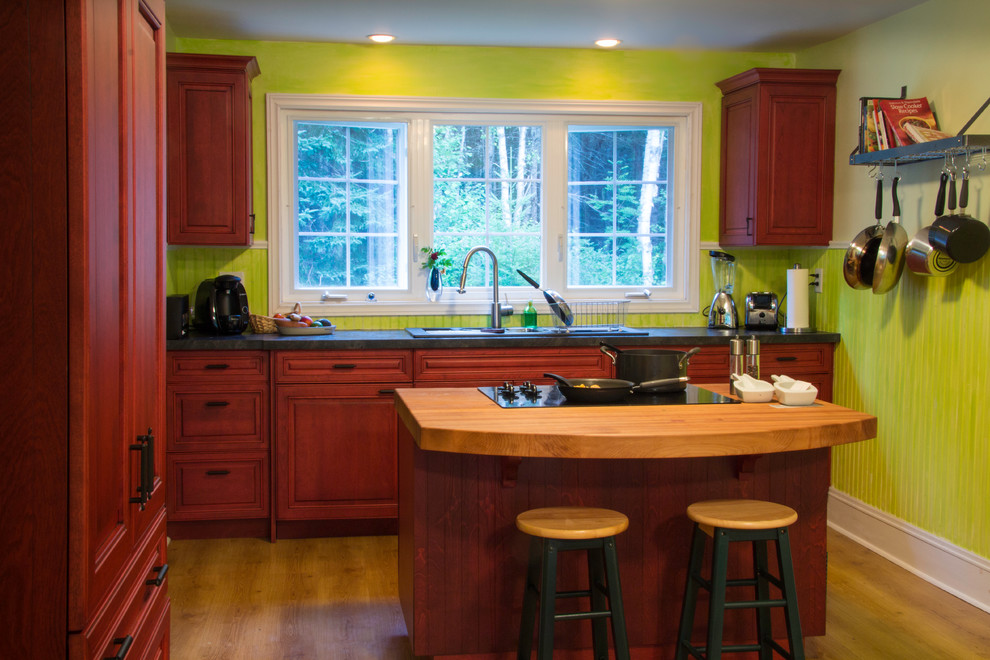 Cette image montre une petite cuisine ouverte parallèle traditionnelle avec un évier 2 bacs, un placard avec porte à panneau surélevé, des portes de placard rouges, un plan de travail en stratifié, une crédence verte et un électroménager noir.