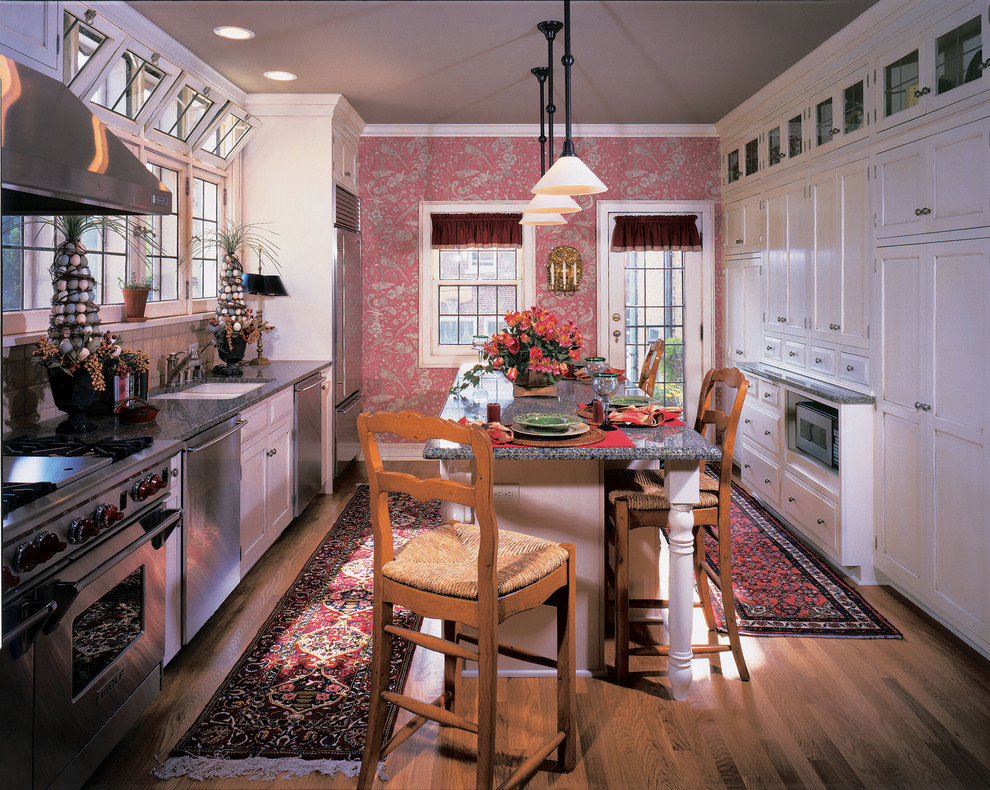 На фото: прямая, отдельная кухня в классическом стиле с техникой из нержавеющей стали, врезной мойкой, фасадами с утопленной филенкой, белыми фасадами и обоями на стенах с
