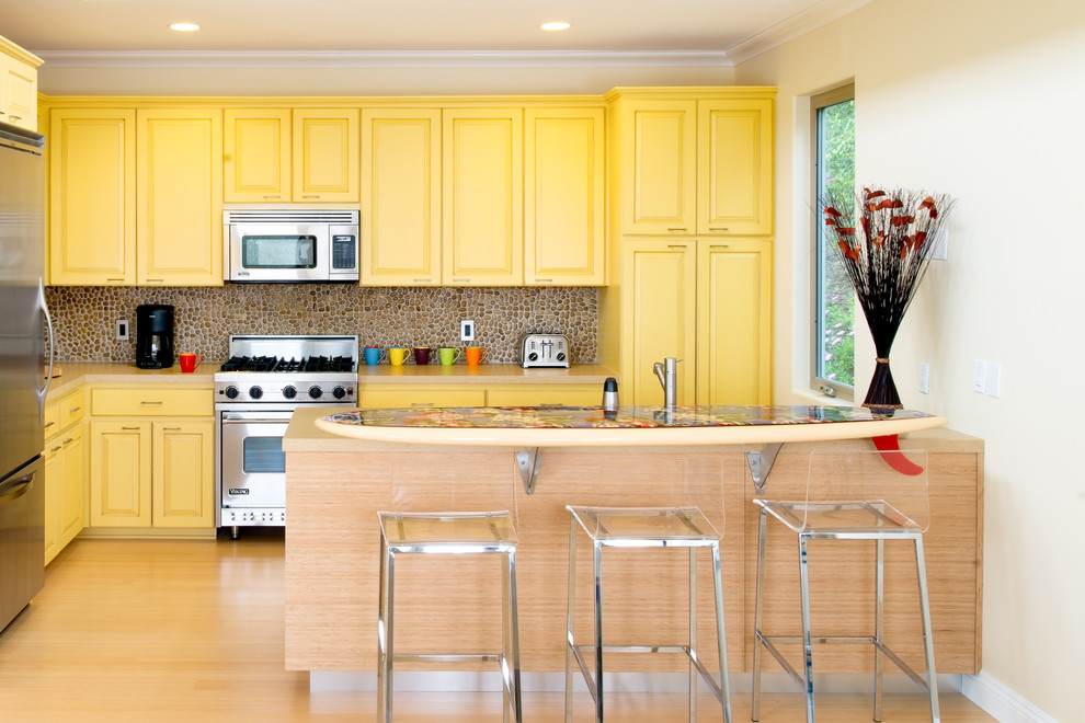 Immagine di una cucina a L tradizionale con ante con bugna sagomata, ante gialle, elettrodomestici in acciaio inossidabile, parquet chiaro e penisola
