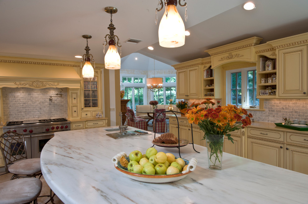 Exempel på ett avskilt, stort klassiskt u-kök, med en undermonterad diskho, luckor med upphöjd panel, gula skåp, marmorbänkskiva, grått stänkskydd, stänkskydd i stenkakel, rostfria vitvaror, en köksö och travertin golv