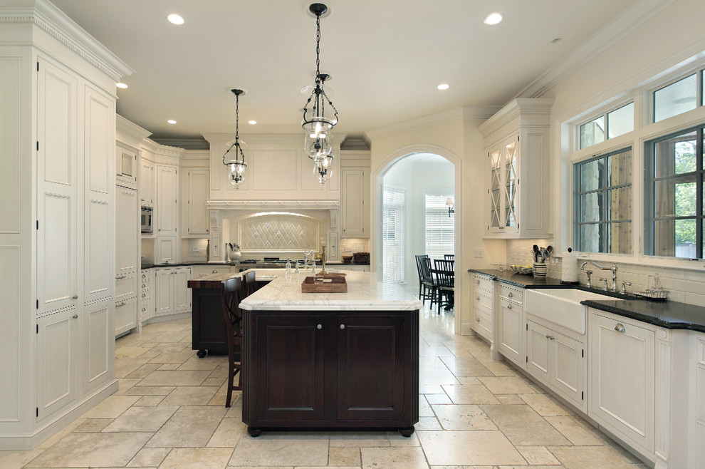Example of a mid-sized classic u-shaped travertine floor eat-in kitchen design in Other with a farmhouse sink, shaker cabinets, white cabinets, marble countertops, beige backsplash, porcelain backsplash, stainless steel appliances and an island