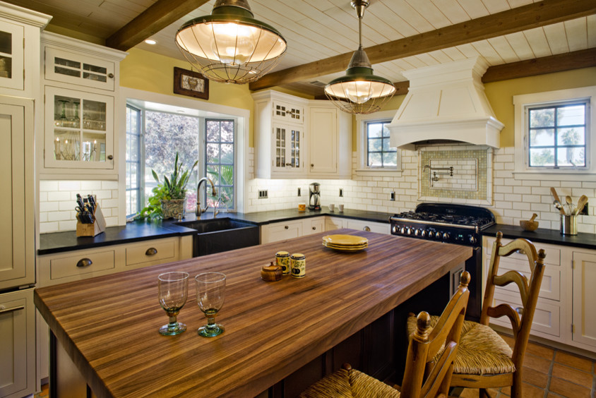 На фото: угловая кухня в классическом стиле с обеденным столом, с полувстраиваемой мойкой (с передним бортиком), фасадами в стиле шейкер, желтыми фасадами, столешницей из известняка, белым фартуком, фартуком из плитки кабанчик и техникой под мебельный фасад
