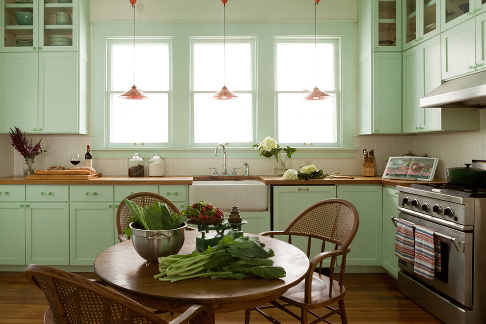 Example of a classic l-shaped medium tone wood floor eat-in kitchen design in Austin with a farmhouse sink, shaker cabinets, green cabinets, wood countertops, beige backsplash, stainless steel appliances and no island