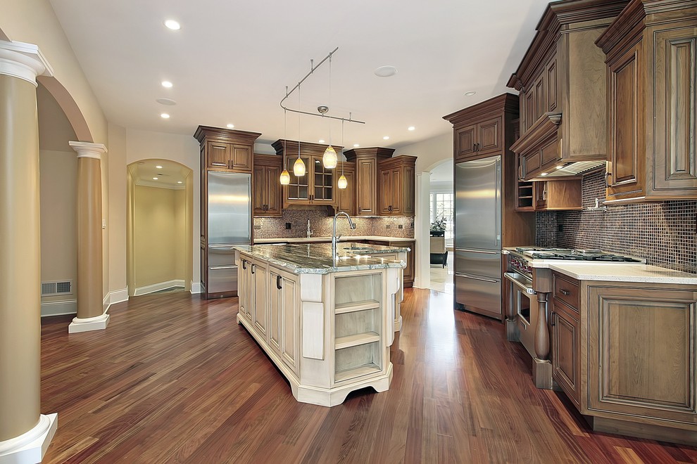Bild på ett stort amerikanskt kök, med en undermonterad diskho, luckor med upphöjd panel, skåp i mellenmörkt trä, bänkskiva i kvartsit, brunt stänkskydd, glaspanel som stänkskydd, rostfria vitvaror, mörkt trägolv och en köksö