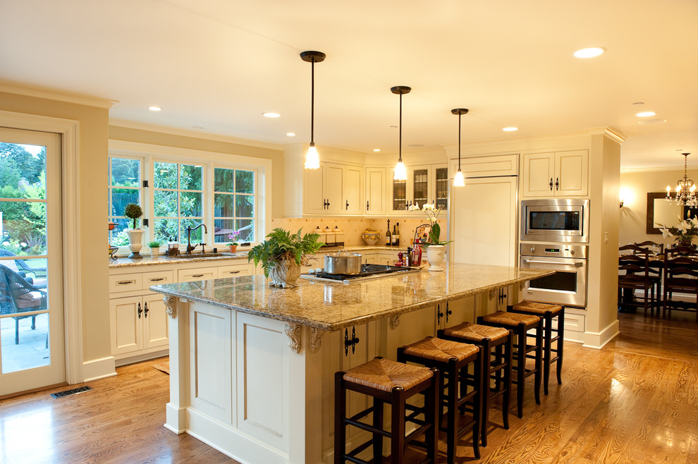 Example of a mid-sized classic l-shaped medium tone wood floor open concept kitchen design in Seattle with beige cabinets, beige backsplash, paneled appliances, ceramic backsplash and an island
