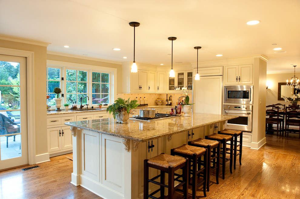 Photo of a medium sized classic l-shaped open plan kitchen in Seattle with beige cabinets, beige splashback, integrated appliances, ceramic splashback, an island and medium hardwood flooring.