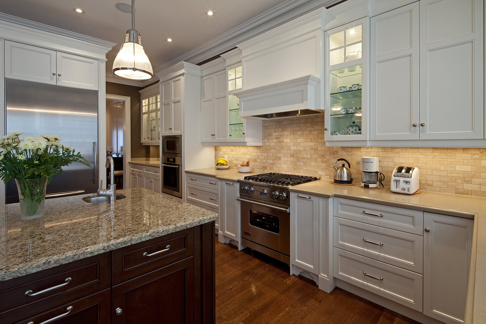 Modelo de cocina clásica con electrodomésticos de acero inoxidable, armarios con paneles empotrados, puertas de armario blancas y salpicadero marrón