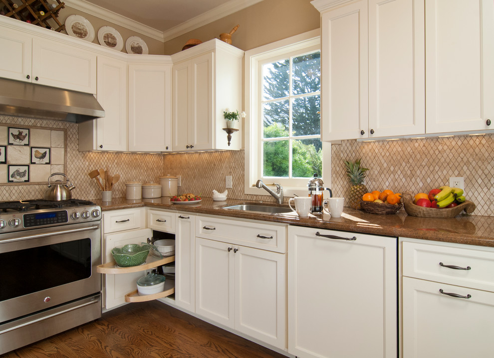 Modelo de cocina tradicional con armarios con paneles empotrados, puertas de armario blancas, salpicadero beige y electrodomésticos de acero inoxidable
