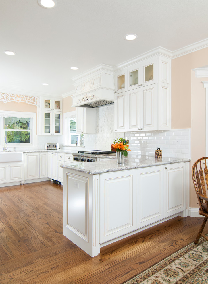 Bild på ett vintage kök och matrum, med en rustik diskho, luckor med upphöjd panel, vita skåp, vitt stänkskydd, stänkskydd i tunnelbanekakel, mörkt trägolv och en halv köksö