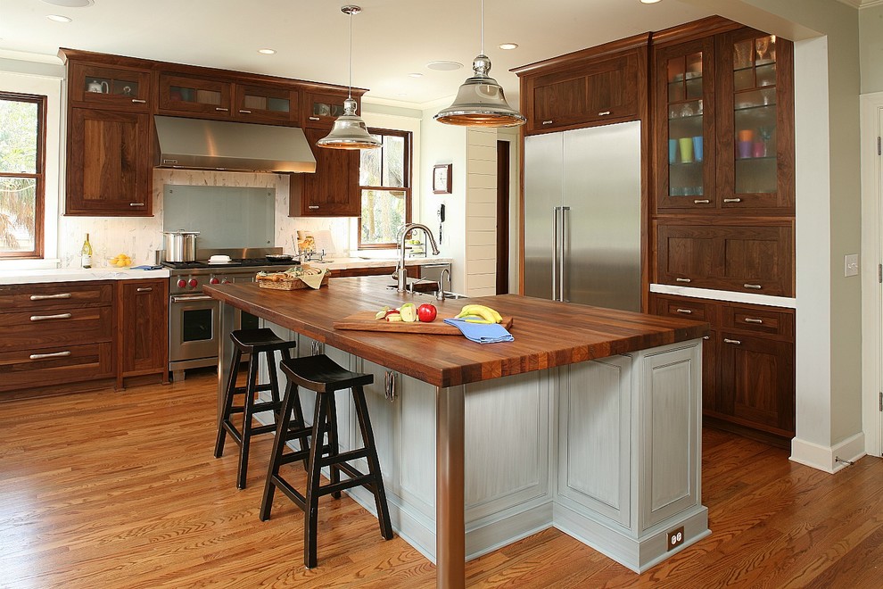 Example of a classic kitchen design in Charleston with glass-front cabinets, stainless steel appliances and wood countertops