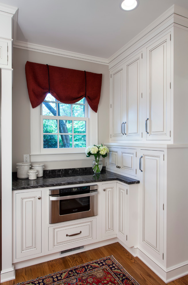 Example of a large transitional u-shaped medium tone wood floor kitchen design in Charlotte with raised-panel cabinets, white cabinets, white backsplash, subway tile backsplash, stainless steel appliances, a double-bowl sink and marble countertops