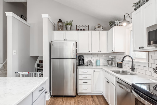White Shaker MDF kitchen cabinets in a bright L-shaped kitchen with subway tile backsplash, quartz countertops, stainless appliances, and black faucet
