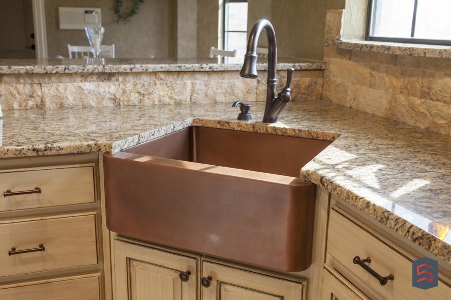 Example of a classic kitchen design in Dallas with a farmhouse sink, raised-panel cabinets, distressed cabinets, granite countertops, beige backsplash and stone tile backsplash