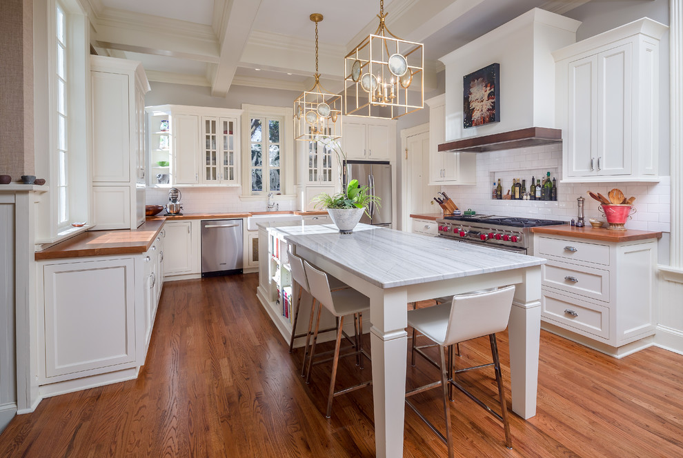 This is an example of a large classic u-shaped kitchen/diner in Atlanta with a belfast sink, white cabinets, white splashback, stainless steel appliances, medium hardwood flooring, an island, shaker cabinets, quartz worktops and metro tiled splashback.