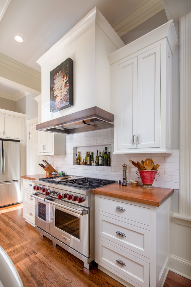 This is an example of a large classic u-shaped kitchen/diner in Atlanta with a belfast sink, white cabinets, white splashback, stainless steel appliances, medium hardwood flooring, an island, shaker cabinets, wood worktops and metro tiled splashback.