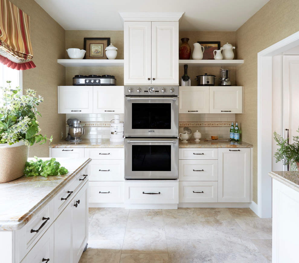 Idées déco pour une cuisine américaine classique en U de taille moyenne avec un évier de ferme, un placard avec porte à panneau surélevé, des portes de placard blanches, un plan de travail en granite, une crédence blanche, une crédence en carrelage métro, un électroménager en acier inoxydable, un sol en travertin, îlot et un sol beige.