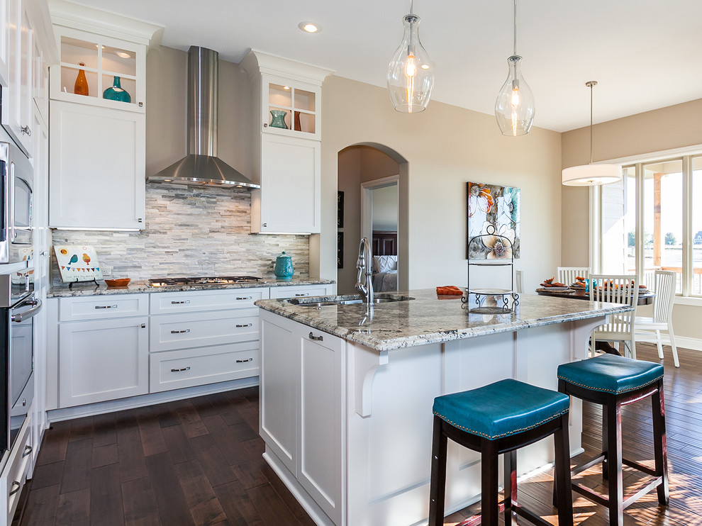 Mid-sized elegant l-shaped dark wood floor eat-in kitchen photo in Wichita with a double-bowl sink, recessed-panel cabinets, white cabinets, granite countertops, gray backsplash, stone tile backsplash, stainless steel appliances and an island