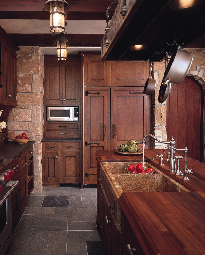 Modelo de cocina clásica con fregadero sobremueble, armarios con paneles empotrados, puertas de armario de madera en tonos medios, encimera de madera y pared de piedra