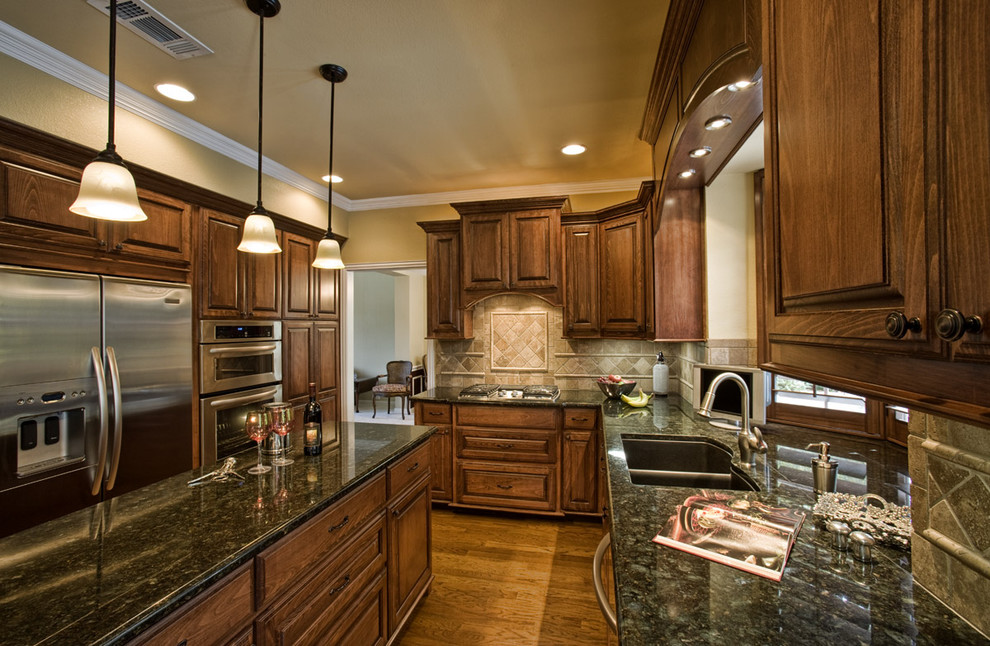 Example of a classic u-shaped enclosed kitchen design in Dallas with stainless steel appliances, a double-bowl sink, raised-panel cabinets, dark wood cabinets, granite countertops, beige backsplash and travertine backsplash