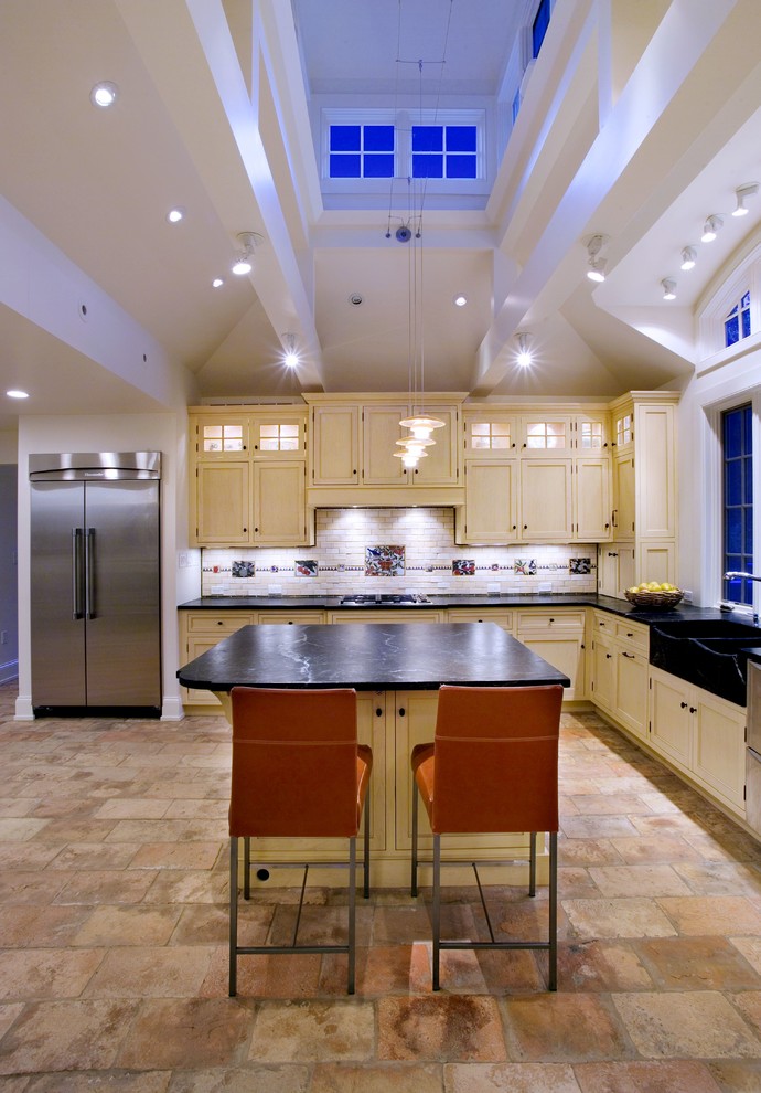 Ejemplo de cocina clásica con electrodomésticos de acero inoxidable, fregadero sobremueble, puertas de armario amarillas y barras de cocina