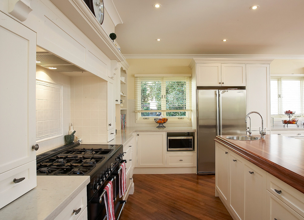 Eat-in kitchen - large traditional u-shaped medium tone wood floor eat-in kitchen idea in Sydney with a single-bowl sink, shaker cabinets, white cabinets, wood countertops, white backsplash, ceramic backsplash and stainless steel appliances