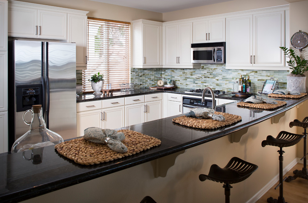 Klassisk inredning av ett mellanstort kök, med luckor med profilerade fronter, vita skåp, granitbänkskiva, blått stänkskydd, stänkskydd i stickkakel, rostfria vitvaror, ljust trägolv och en halv köksö