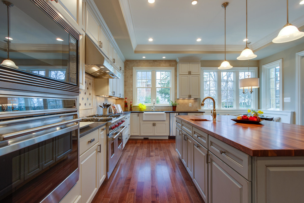 На фото: угловая кухня в классическом стиле с с полувстраиваемой мойкой (с передним бортиком), фасадами с выступающей филенкой, белыми фасадами и деревянной столешницей