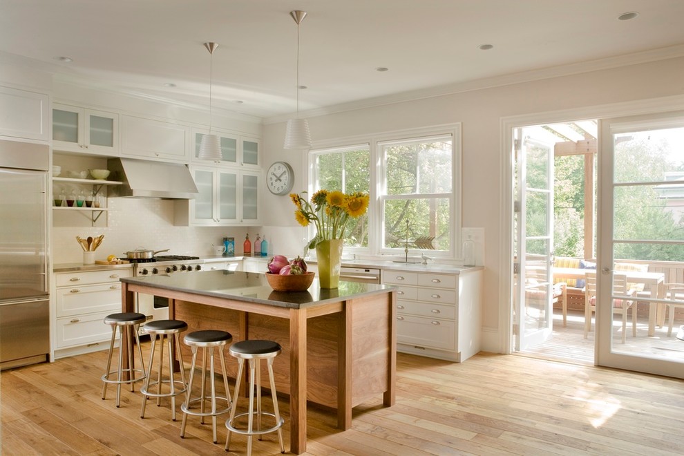 Foto di una cucina chic di medie dimensioni con ante di vetro, ante bianche, top in superficie solida, parquet chiaro, paraspruzzi bianco e elettrodomestici in acciaio inossidabile
