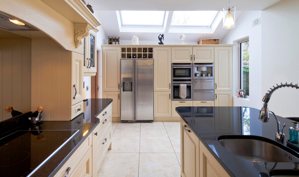 Large traditional single-wall open plan kitchen in Dublin with a double-bowl sink, raised-panel cabinets, white cabinets, quartz worktops, stainless steel appliances, porcelain flooring and an island.