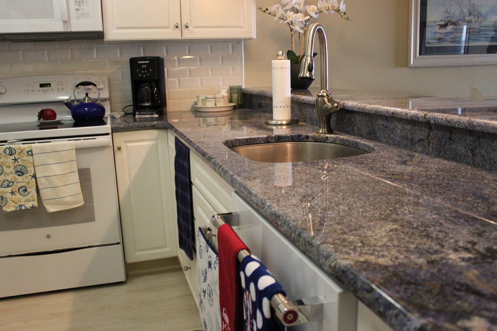 Photo of a traditional u-shaped kitchen in New York with a single-bowl sink, raised-panel cabinets, white cabinets, granite worktops, white splashback, metro tiled splashback, a breakfast bar and blue worktops.
