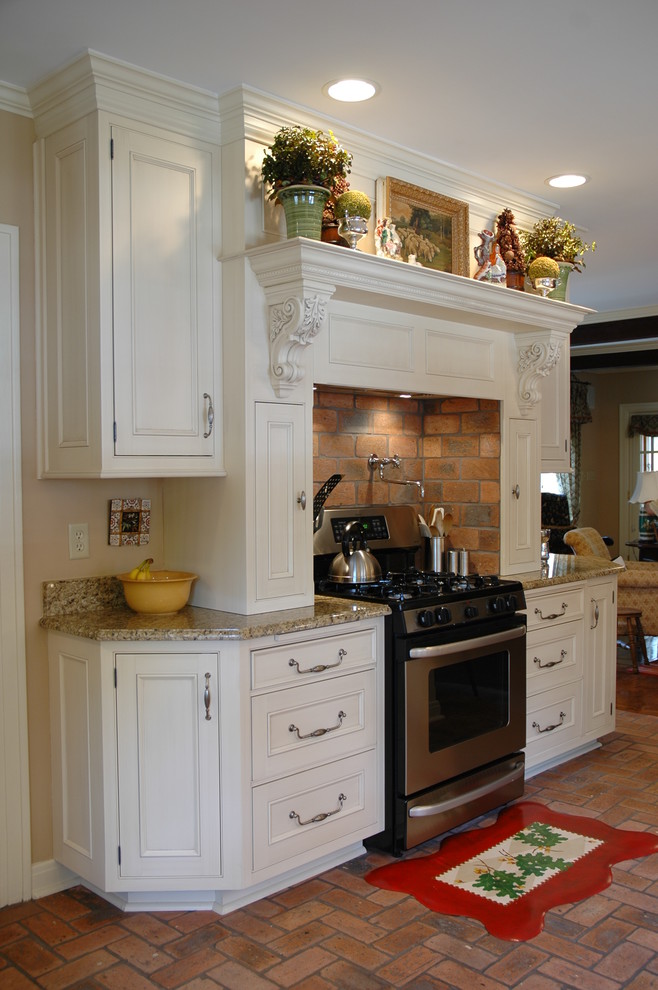 Modelo de cocina clásica con fregadero sobremueble, armarios con paneles empotrados, puertas de armario blancas, encimera de laminado, electrodomésticos con paneles y suelo de ladrillo