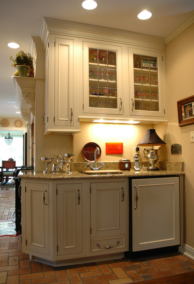 Klassisk inredning av ett kök, med en integrerad diskho, luckor med infälld panel, gula skåp, granitbänkskiva, integrerade vitvaror och tegelgolv
