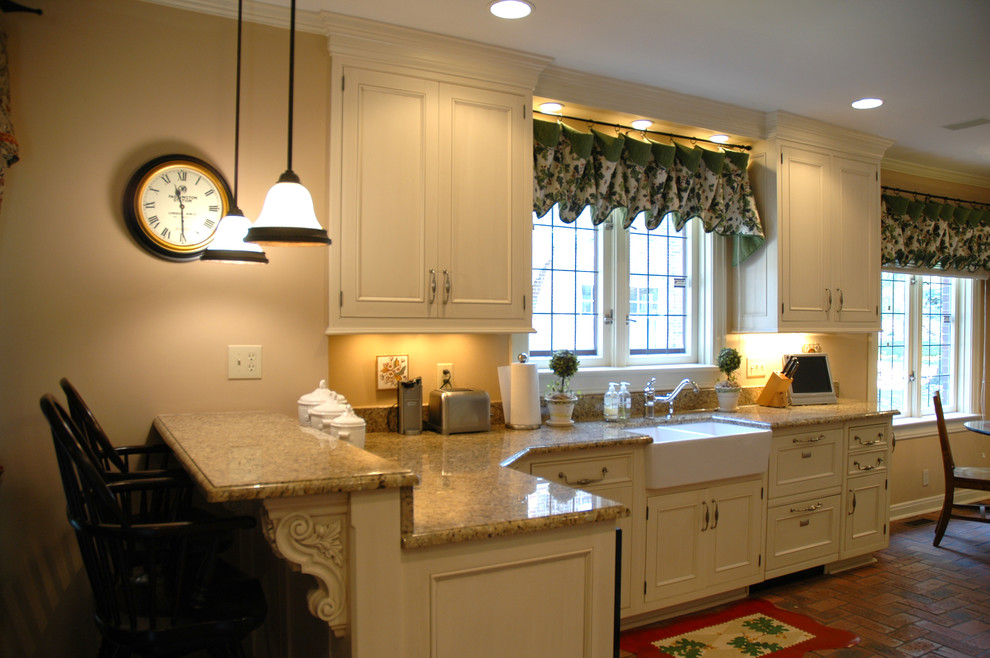Inredning av ett klassiskt kök, med en integrerad diskho, luckor med infälld panel, gula skåp, granitbänkskiva, integrerade vitvaror, tegelgolv och gult stänkskydd