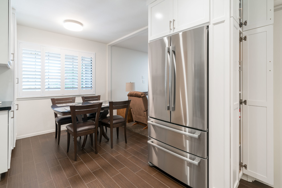 Mid-sized elegant l-shaped dark wood floor and brown floor eat-in kitchen photo in Other with a double-bowl sink, shaker cabinets, white cabinets, granite countertops, black backsplash, subway tile backsplash, stainless steel appliances, an island and black countertops