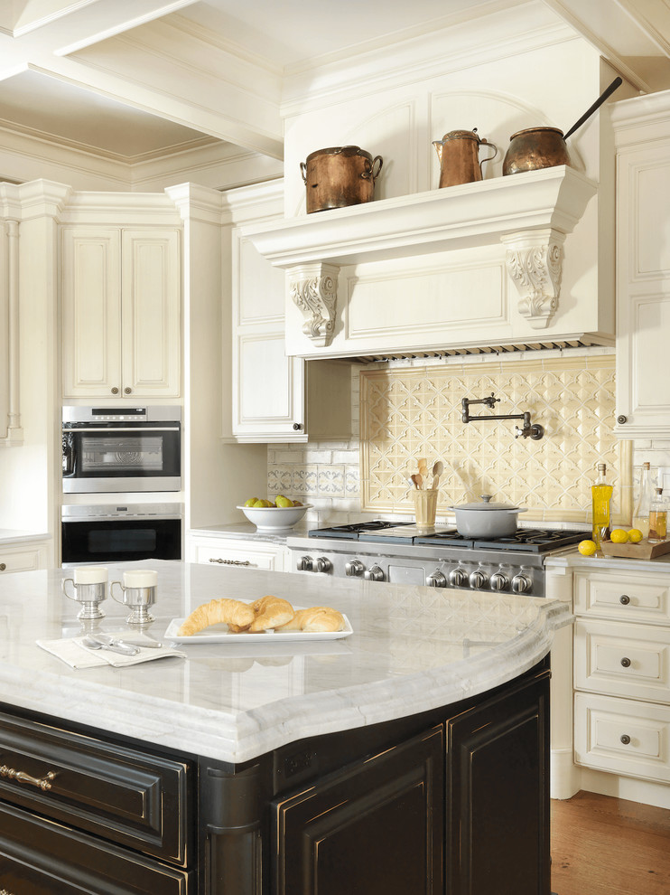 Klassisk inredning av ett u-kök, med luckor med upphöjd panel, beige skåp, bänkskiva i kvartsit, beige stänkskydd, rostfria vitvaror, mellanmörkt trägolv och flera köksöar