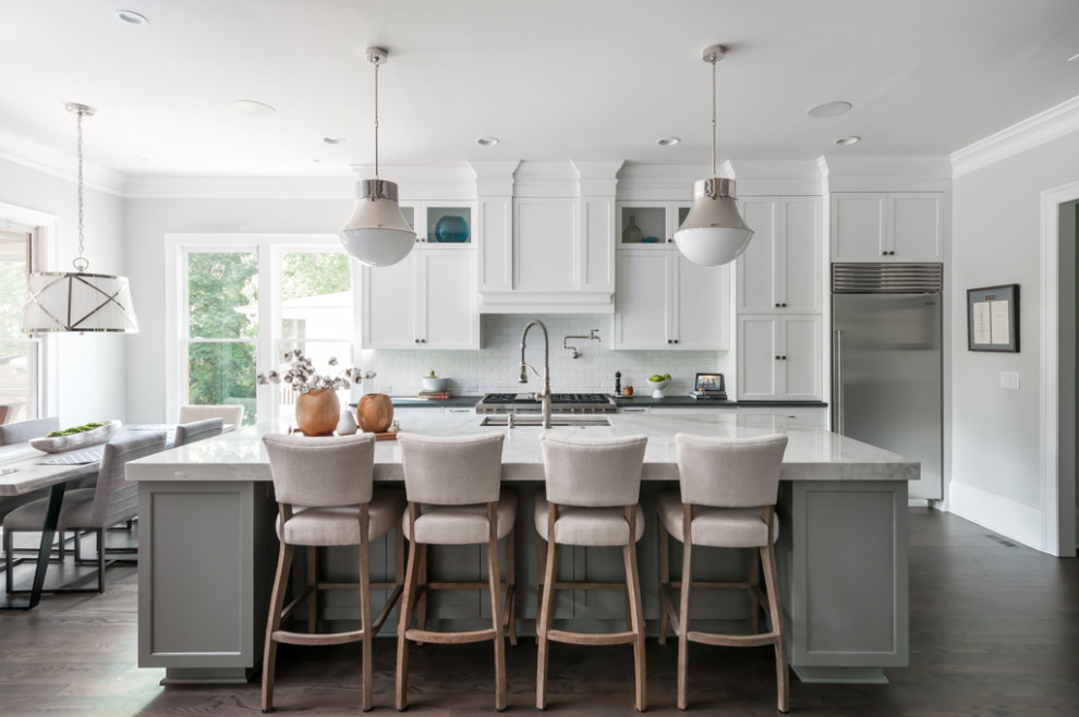 Foto de cocina comedor tradicional renovada grande con fregadero de un seno, armarios estilo shaker, puertas de armario blancas, encimera de cuarcita, salpicadero blanco, electrodomésticos de acero inoxidable, una isla, suelo marrón, suelo de madera oscura y encimeras negras