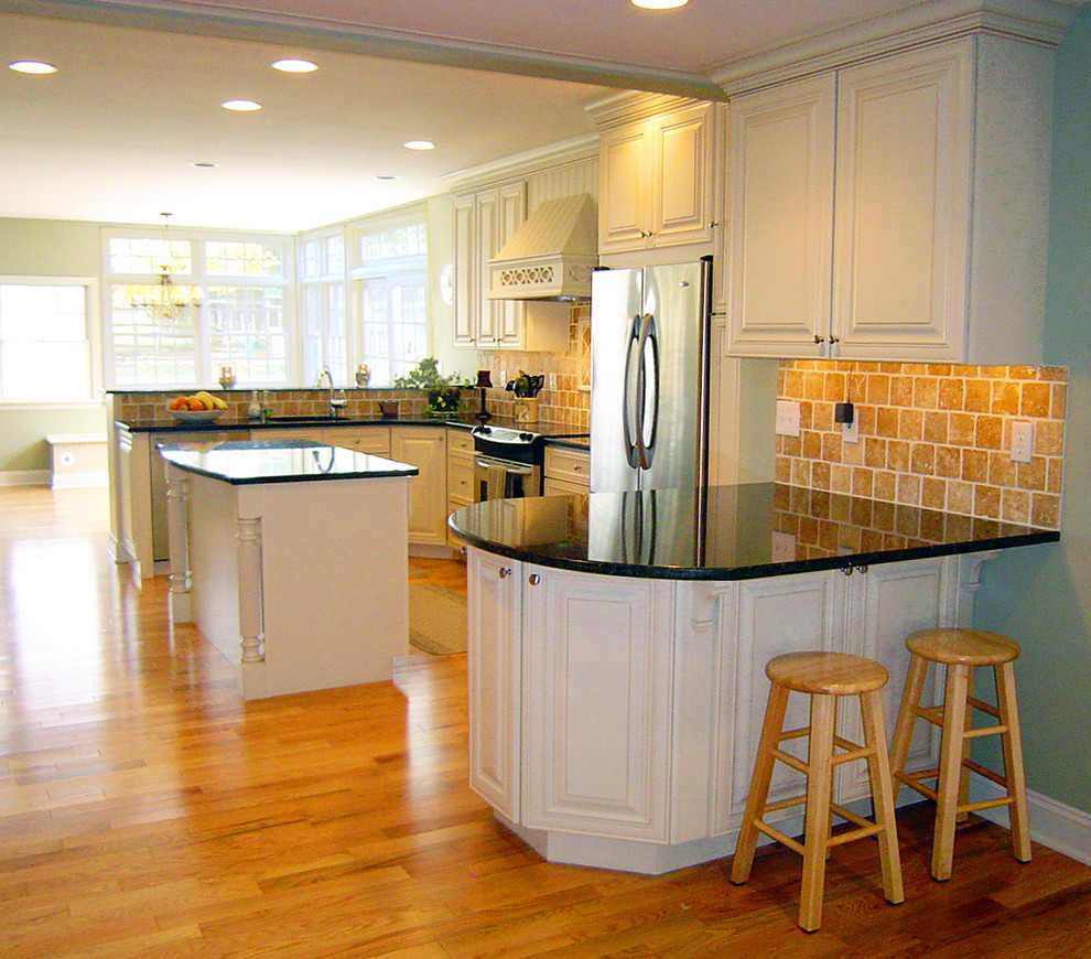 Inspiration for a large timeless u-shaped medium tone wood floor eat-in kitchen remodel in Philadelphia with stainless steel appliances, an undermount sink, raised-panel cabinets, white cabinets, granite countertops, beige backsplash, stone tile backsplash and an island